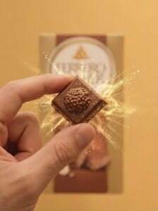 Mano che regge un singolo quadrotto di cioccolato Ferrero Rocher mostrandone le dimensioni e il dettaglio della forma.