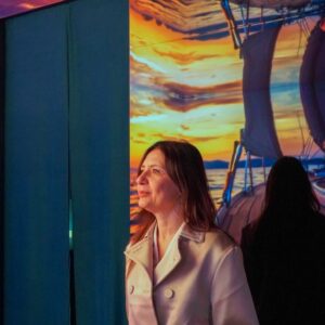 Installazione immersiva Vette e Onde: visitatrice osserva una proiezione di tramonto su barca a vela creata con AI generativa2
