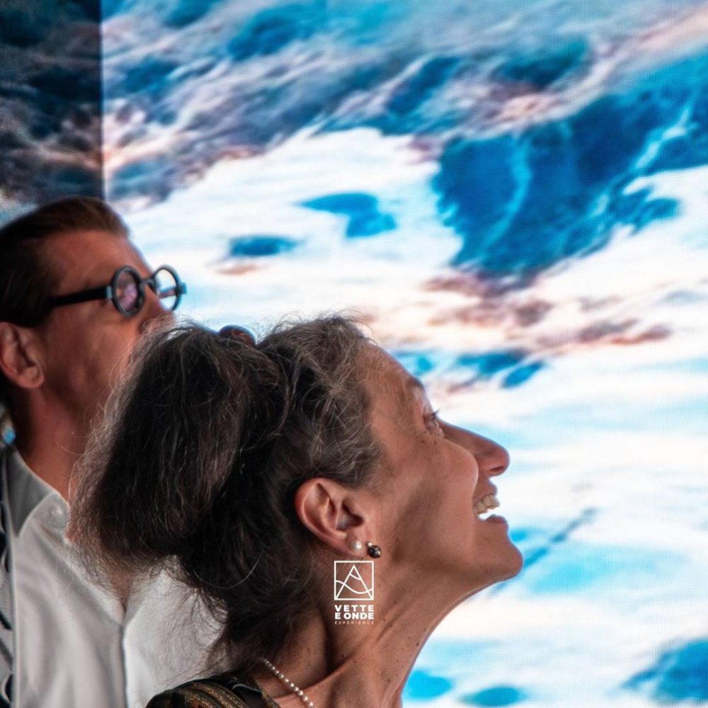 Installazione immersiva Vette e Onde: visitatrice osserva una proiezione di tramonto su barca a vela creata con AI generativa3