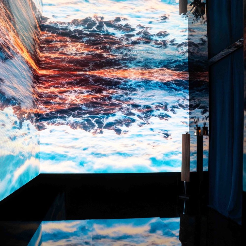 Installazione immersiva Vette e Onde: visitatrice osserva una proiezione di tramonto su barca a vela creata con AI generativa1