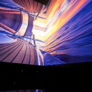 Installazione immersiva Vette e Onde: visitatrice osserva una proiezione di tramonto su barca a vela creata con AI generativa8